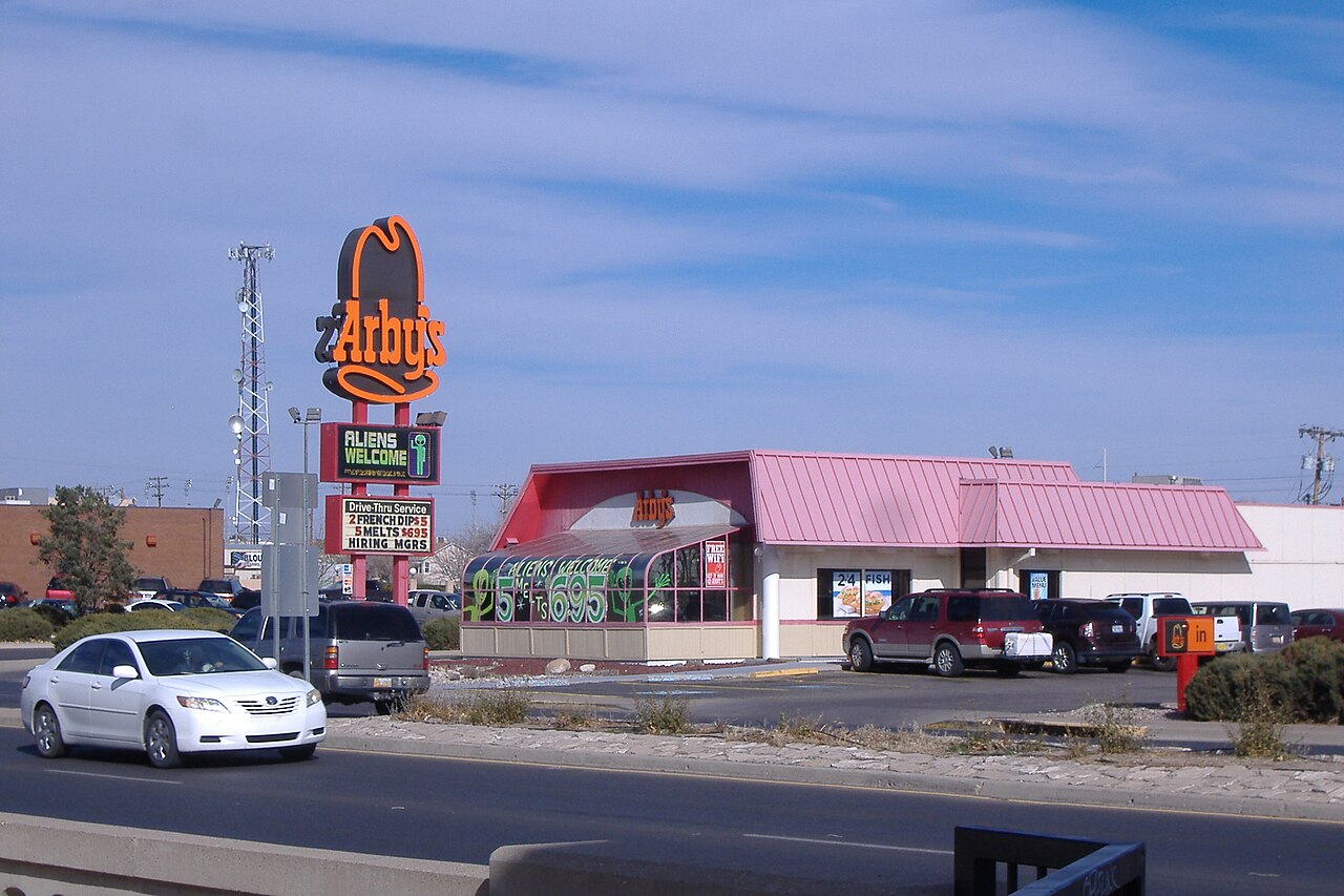 An Arby's whose roadside sign reads ALIENS WELCOME beside a green alien figure